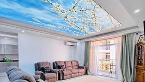 Uma sala de estar moderna com um grande mural no teto, um conjunto de sofás e uma mesa de centro de vidro.