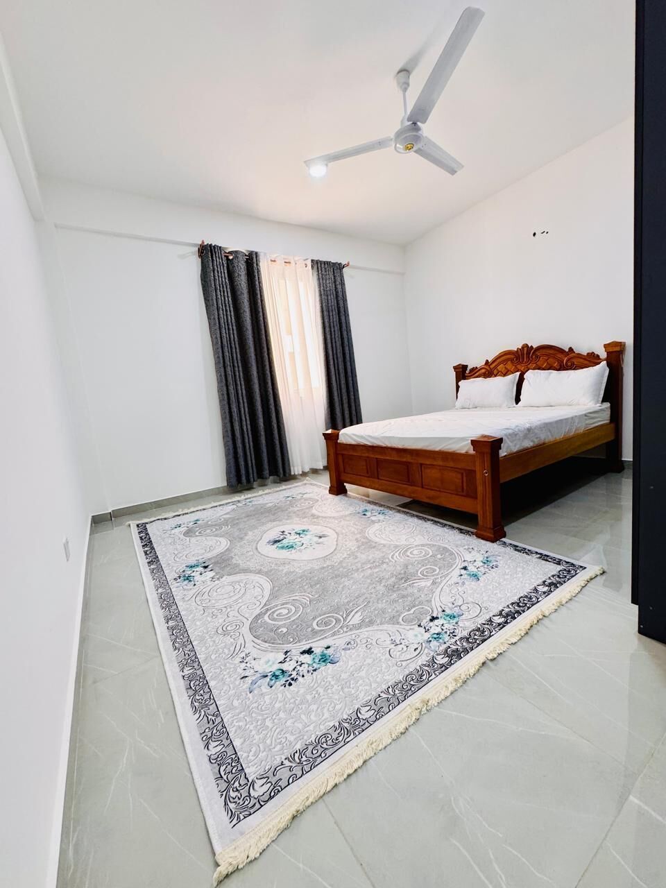 A bedroom with a bed, a ceiling fan, and a patterned rug.