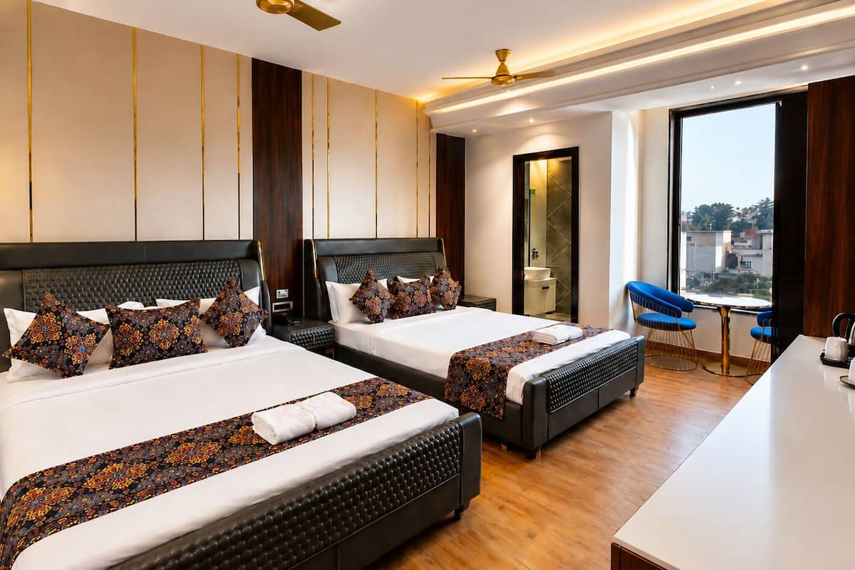 Quarto de hotel com duas camas, uma escrivaninha, uma cadeira, um ventilador de teto e vista para a cidade.
