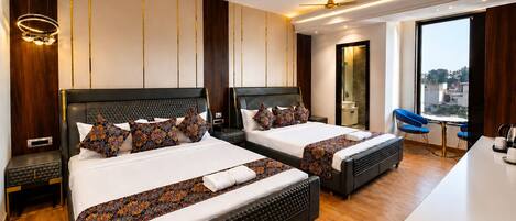 A hotel room with two beds, a desk, a chair, a ceiling fan, and a view of the city.