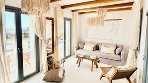 Een ruime woonkamer met een houten plafond, een zithoek, een salontafel en een rieten stoel.