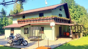 Una casa de dues plantes amb un balcó, un trampolí i una moto aparcada al davant.