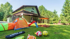 Una casa amb façana verda, un trampolí, una tenda i un tobogan al jardí.