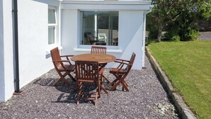 A white building with a patio area featuring a round wooden table and four chairs. - Teach Feirme (Clonakilty)
