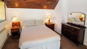 A bedroom with a bed, two bedside tables with lamps, a dresser, a mirror, and a wooden ceiling. - Teach Feirme (Clonakilty)