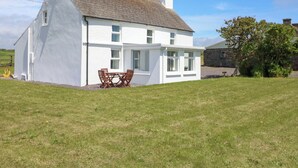 A white house with a sloped roof, a chimney, and a small patio with a table and chairs. - Teach Feirme (Clonakilty)