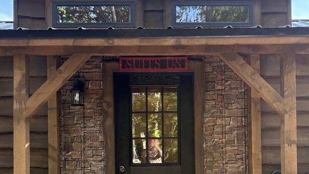 A rustic wooden building with a stone facade, a wooden porch, and a sign above the door.