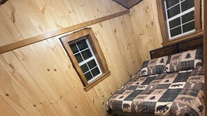 A wooden cabin bedroom with a bed, a window, and a wooden bench.