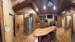 A wooden cabin interior with a kitchen, dining area, and a sofa.
