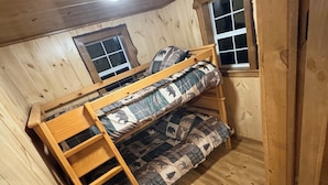A bunk bed with a ladder, wooden walls, and two windows.