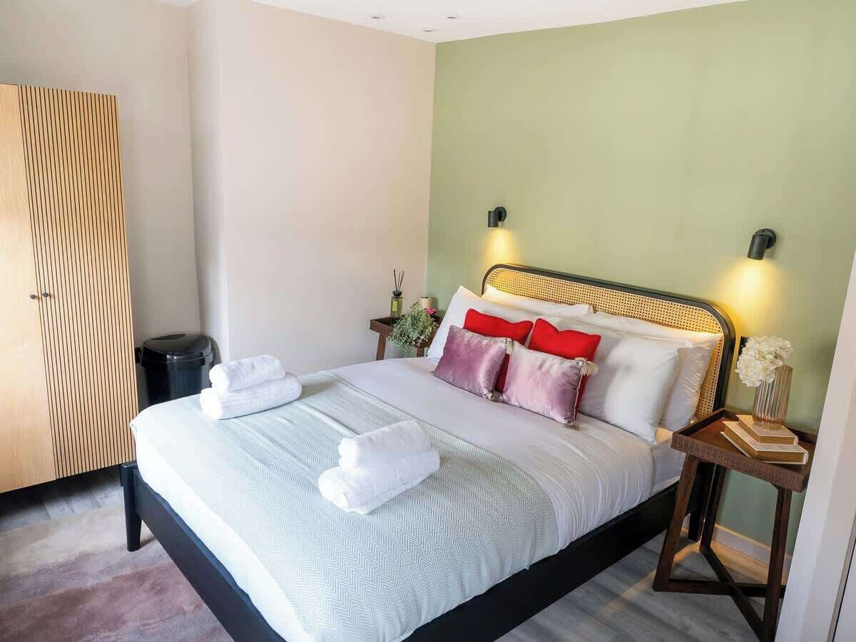 A neatly made bed with pillows and towels, a bedside table with a book and a vase, and a wardrobe in a hotel room.