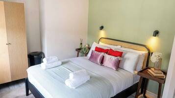 A neatly made bed with pillows and towels, a bedside table with a book and a vase, and a wardrobe in a hotel room.