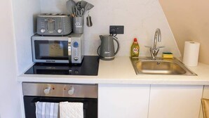 A compact kitchenette with a GEERAS microwave, two toasters, a kettle, and a sink with a faucet.