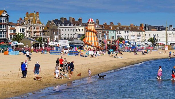 A beach with people, a large striped tower, and buildings in the background.