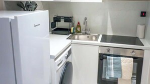 Une cuisine compacte équipée d’un four encastré, d’un lave-linge et d’un évier.