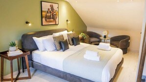 Ein Schlafzimmer mit einem Bett, einem Nachttisch, einem Sessel, einem kleinen Tisch mit Pflanze und einem Wandbild.