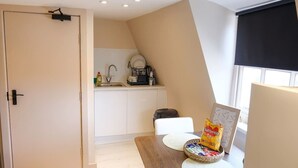 Eine kleine Küche mit Spüle, einer Kaffeemaschine und einem Fenster mit Jalousie.