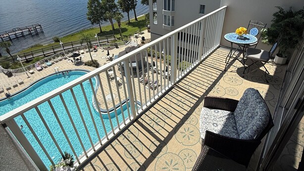 A balcony with a view of a swimming pool and a lake, outdoor furniture, and a building with balconies. - Peaceful Lakefront unit near Disney and Universal (Orlando)