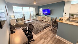 A modern living room with a large window, a flat-screen TV, a dining area, and a kitchen. - Peaceful Lakefront unit near Disney and Universal (Orlando)