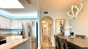 A modern kitchen with a stainless steel refrigerator, a dining area with a wooden table and chairs, and a hallway leading to another room. - Peaceful Lakefront unit near Disney and Universal (Orlando)