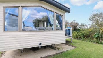 A caravan with a large window, a visible bed, and a garden area.