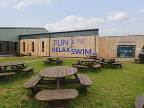 Ein Außenpoolbereich mit Picknicktischen und einem Holzgebäude mit Schildern für eine entspannte und vergnügliche Schwimmmöglichkeit.