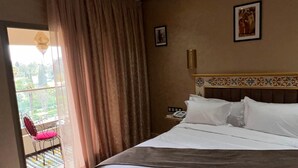 Ein Hotelzimmer mit einem großen Bett, einem Sessel, einem Nachttisch mit Telefon und Blick ins Freie.