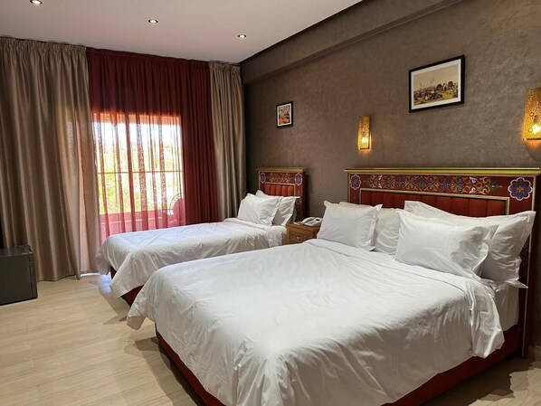 A hotel room with two beds, a desk, and a window with curtains.