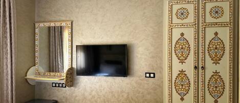 A hotel room with a flat-screen TV mounted on the wall, a small cabinet below it, and a wardrobe with intricate designs.