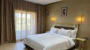 A hotel room with a large bed, curtains, a headboard with a decorative design, wall-mounted lights, and a framed picture.