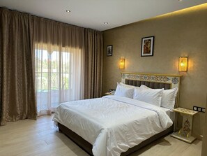 Habitación de hotel con una cama grande, cortinas, cabecero con diseño decorativo, luces fijadas a la pared y un cuadro enmarcado.