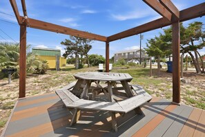 Um gazebo de madeira com uma mesa redonda e bancos, cercado por um deck.