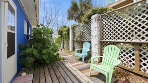Een houten terras met twee Adirondack-stoelen, een blauw gebouw en een wit lattenhek.