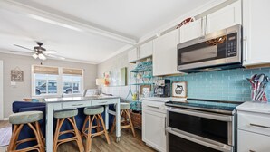 Een keuken met een centraal eiland, barkrukken, een magnetron, oven en een plafondventilator.