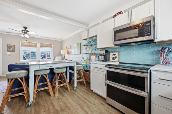 A kitchen with a central island, bar stools, a microwave, oven, and a ceiling fan. - Hatfield's Hideaway | A Classic EI Cottage! (Emerald Isle)