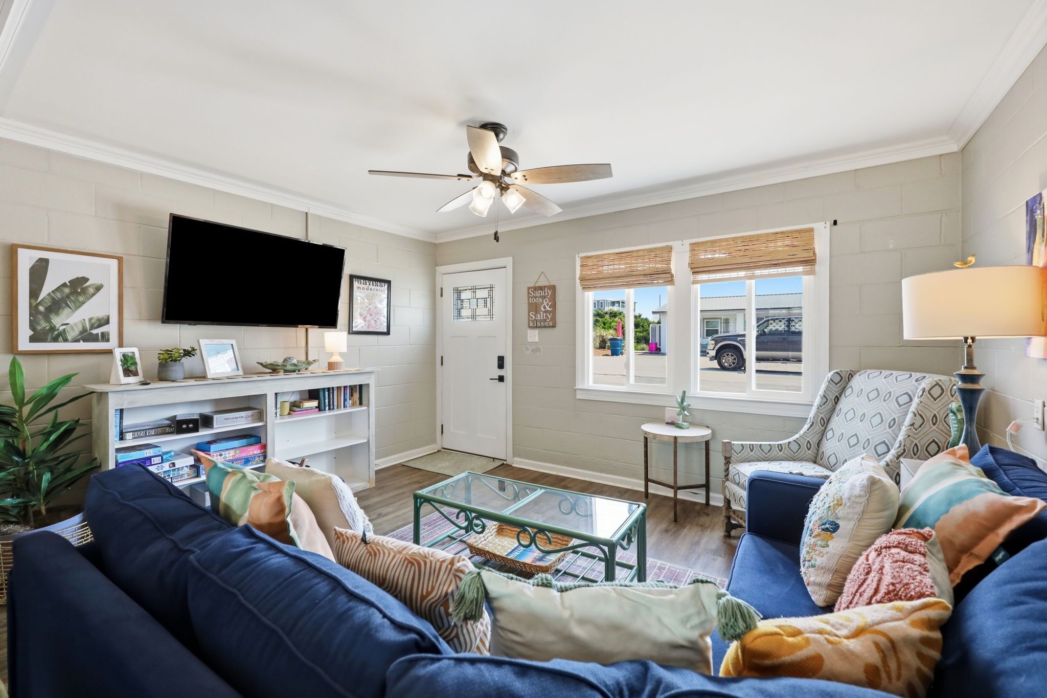 A living room with a blue sofa, a glass coffee table, a ceiling fan, a TV, and a bookshelf.