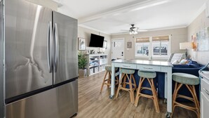 Een moderne keuken met een roestvrijstalen koelkast, een eethoek met barkrukken, een plafondventilator en een aan de muur bevestigde televisie.