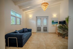 A living room with a sofa, a ceiling fan, a painting, and a plant. - Villa Flora (Jolly Harbour)