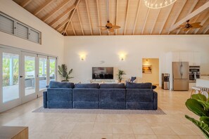 A spacious living area with a large sofa, ceiling fans, a flat-screen TV, and a kitchen with modern appliances. - Villa Flora (Jolly Harbour)
