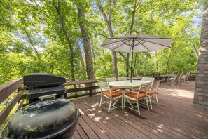 Een terras met een barbecue, tafel, stoelen en een parasol.