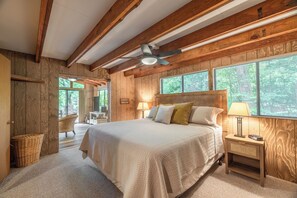 Een slaapkamer met een groot bed, houten wanden, een plafondventilator en een raam met jaloezieën.