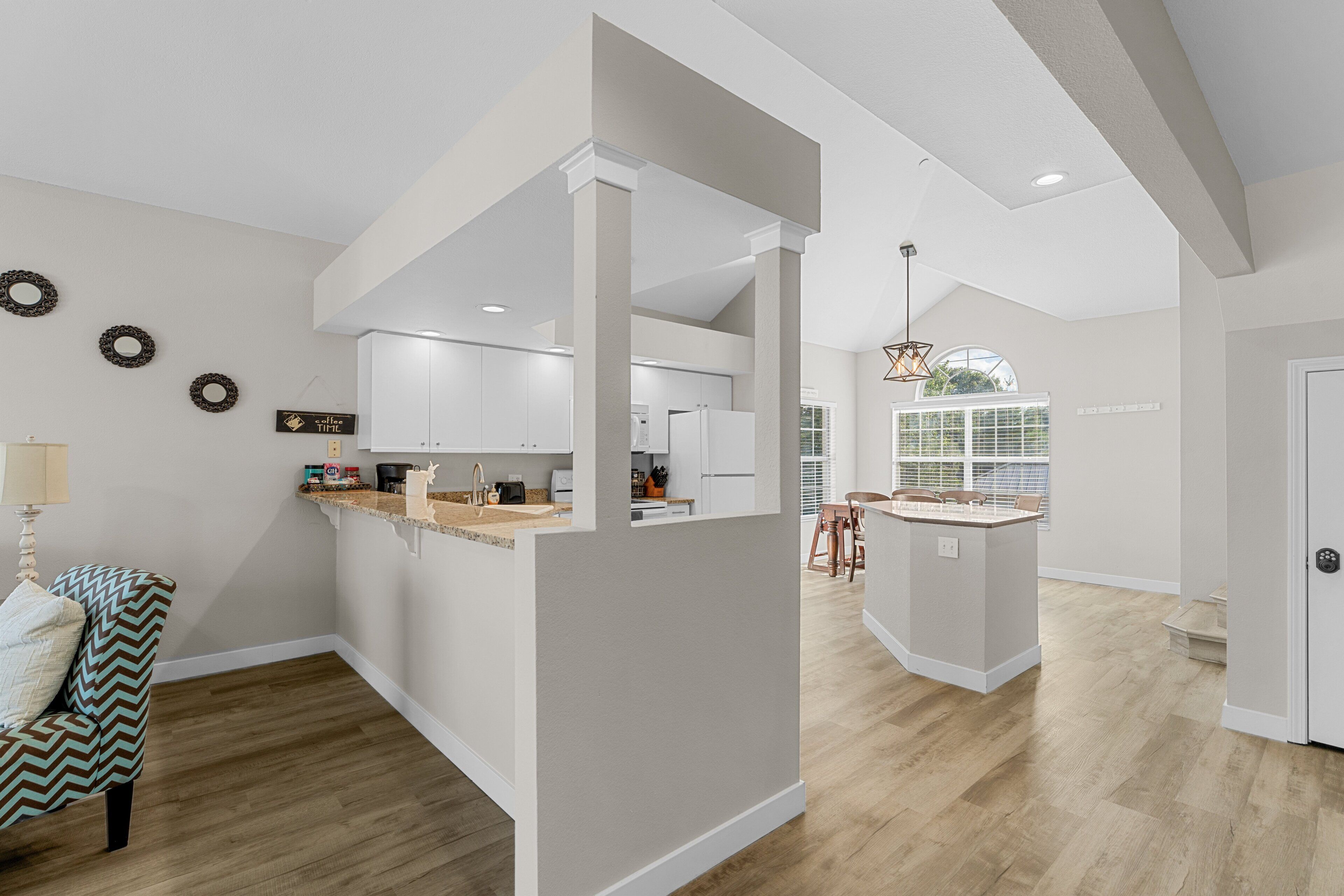 A modern kitchen with white cabinets, a central island, and a dining area with bar stools.