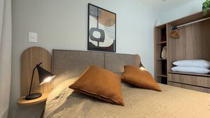 A modern bedroom with a bed, two bedside lamps, a headboard, a wall-mounted artwork, and a wooden wardrobe. - GA 22 Ape com AR prox. Allianz e A (São Paulo)