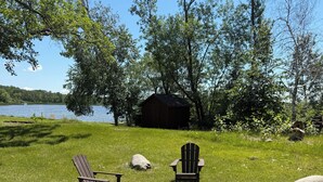 A lakeside setting with Adirondack chairs, a fire pit, and a small shed.