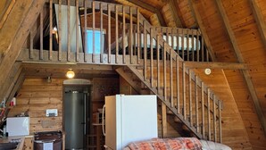 A loft-style room with a wooden staircase, a sofa, a table, and a refrigerator.