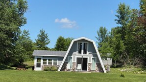 A house with a stone foundation, a sloped roof, and a front porch with two chairs.