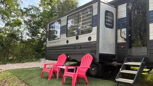 En autocamper med et overdækket område foran, to røde Adirondack-stole og en lille trappeopgang til indgangen.