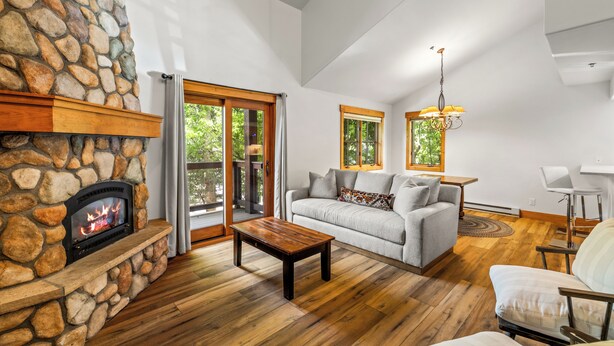 A living room with a stone fireplace, a sofa, a coffee table, and a chandelier. - Mountain Comfort Between Downtown and the Slopes – Pines at Ore House 201! (Steamboat Springs)