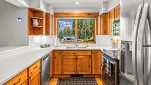 A modern kitchen with wooden cabinets, a stainless steel refrigerator, and a window with a view of trees. - Mountain Comfort Between Downtown and the Slopes – Pines at Ore House 201! (Steamboat Springs)
