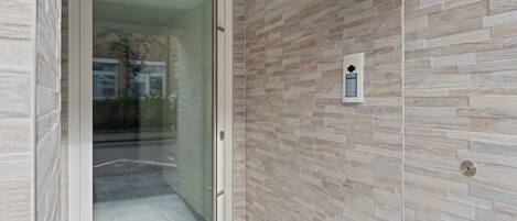 A modern interior with a glass door leading to a hallway, a patterned wall, and a small control panel.